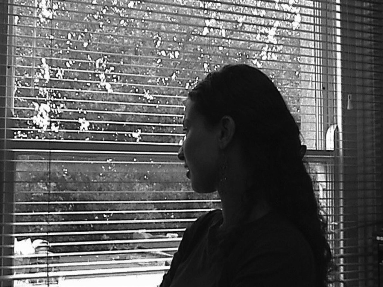 A woman standing at a window looking out of a blind