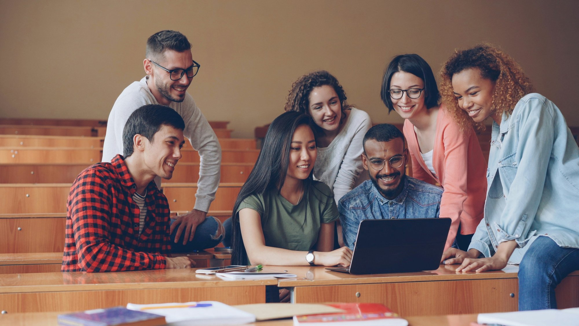A group of people crowd around a laptop screen smiling.