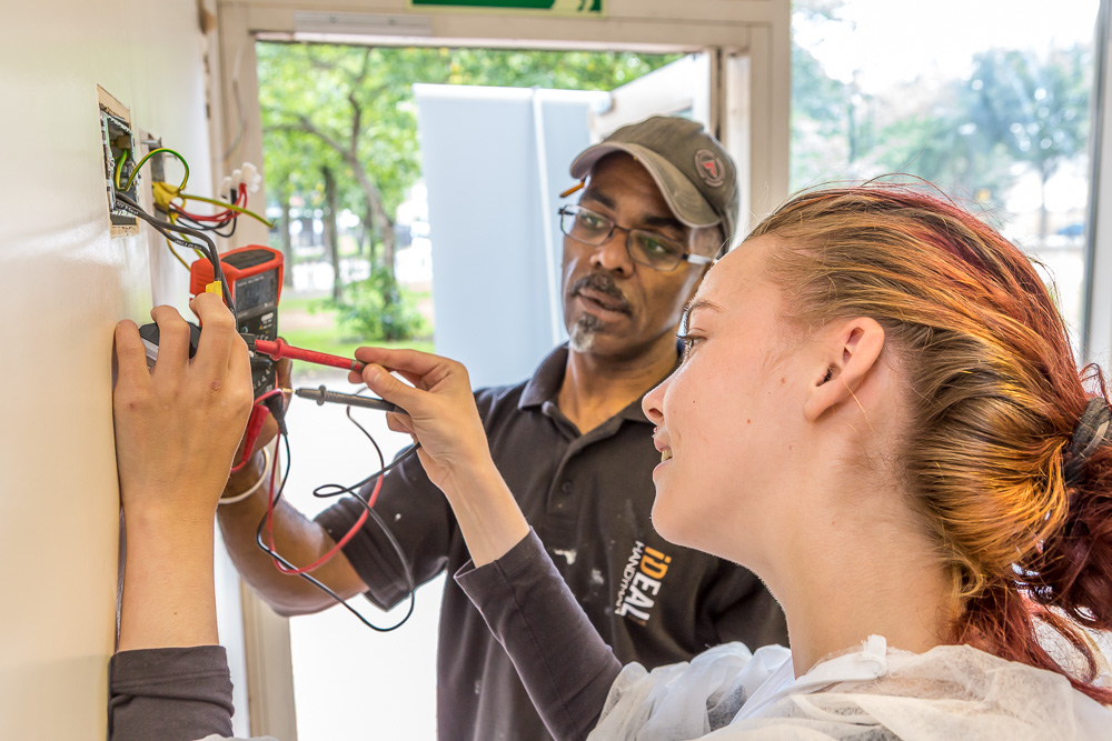 A black man teaching a white young girl how to wire a fuse box