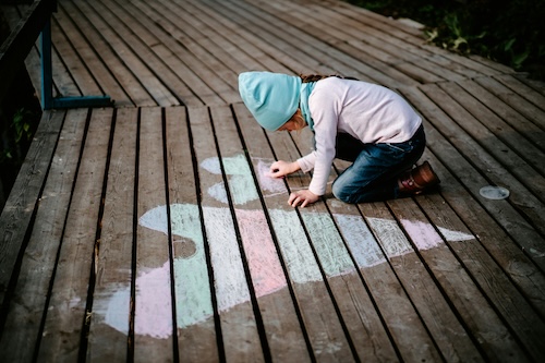 Child drawing hearts on decking with pastel chalks