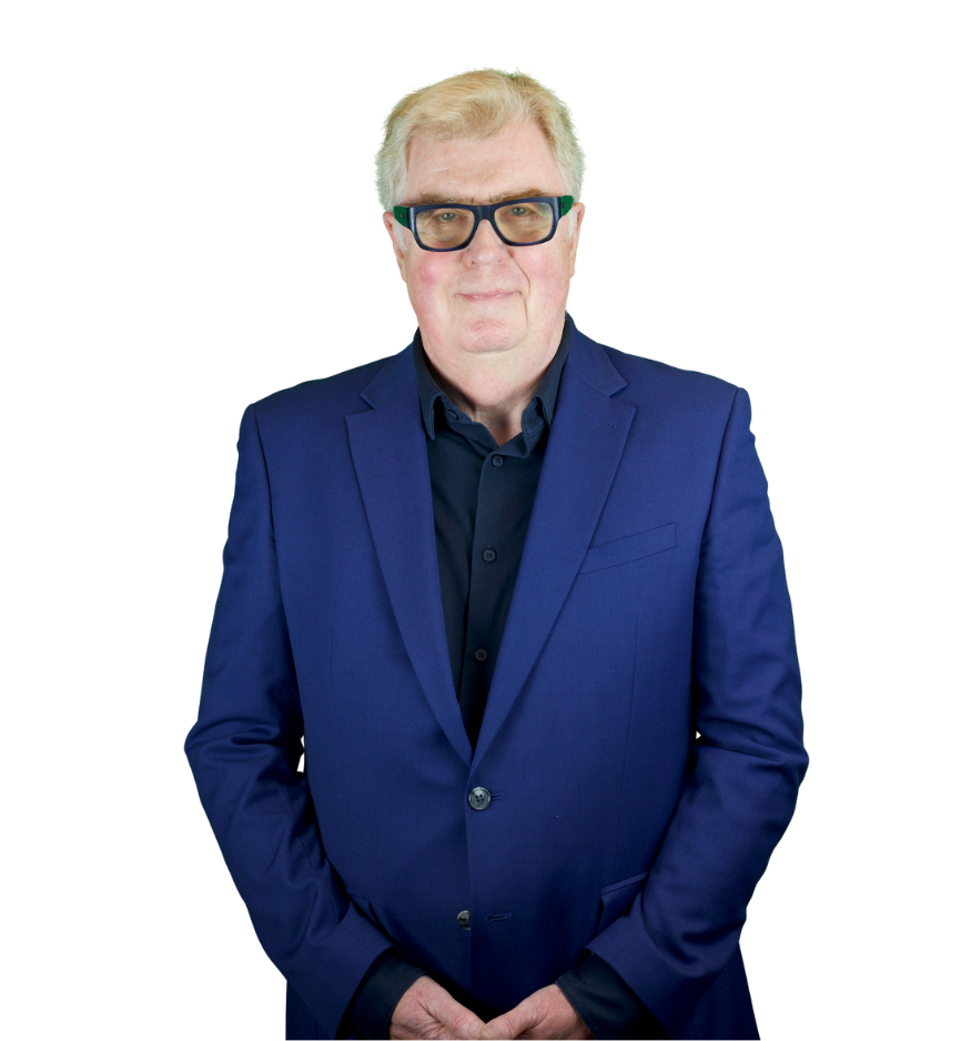 Trustee Gareth wears a blue blazer over a black shirt. He wears a pair of black framed glasses.