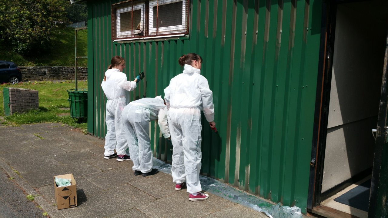 Three people painting a shed wall green