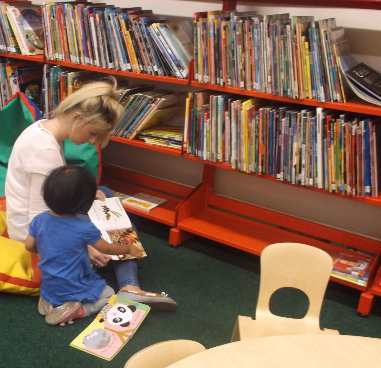 A woman helping a child read in a library